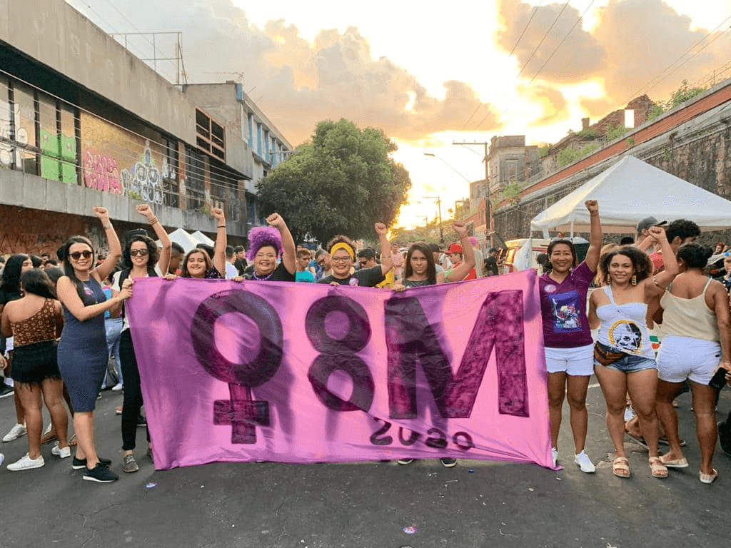 Grupo de mulheres com o braço direito erguido e segurando uma faixa escrito ''8M 2020'' Dia da Mulher carreata em Manaus