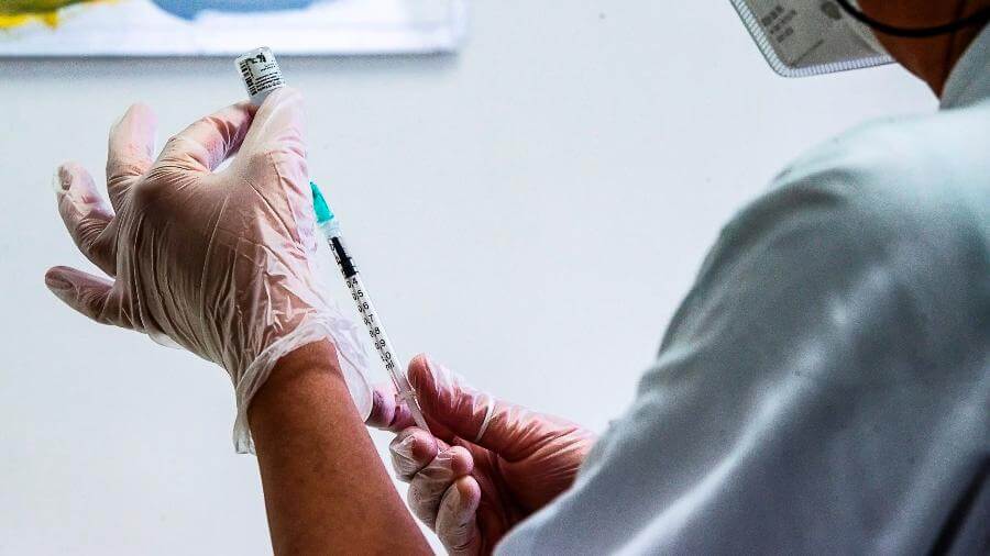 Mãos enluvadas e segurando uma vacina
